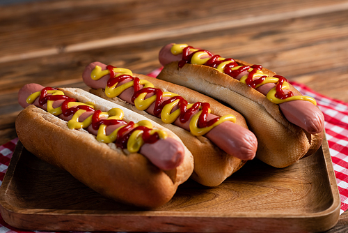 close up view of hot dogs with mustard and ketchup near plaid napkin on wooden surface