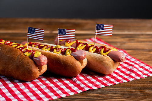 delicious hot dogs with small american flags and checkered napkin on wooden table isolated on grey