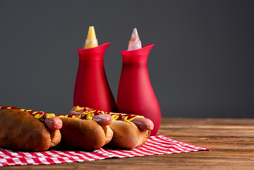 blurred sauce bottles near tasty hot dogs on plaid napkin isolated on grey