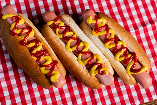 top view of delicious hot dogs with mustard and ketchup on plaid tablecloth