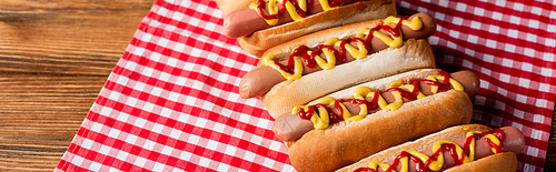 hot dogs with mustard and ketchup on plaid napkin and wooden table, banner