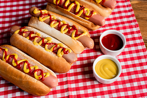 delicious hot dogs near ketchup and mustard on checkered napkin and wooden table