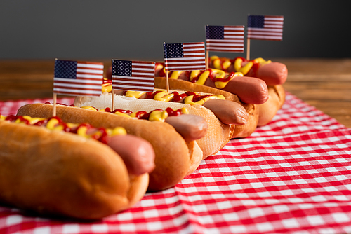 tasty hot dogs with sauces and small american flags on checkered table napkin isolated on grey