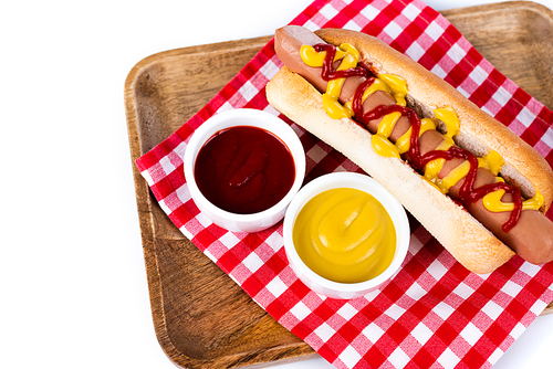 tasty hot dog with mustard and ketchup on plaid table napkin and wooden tray isolated on white