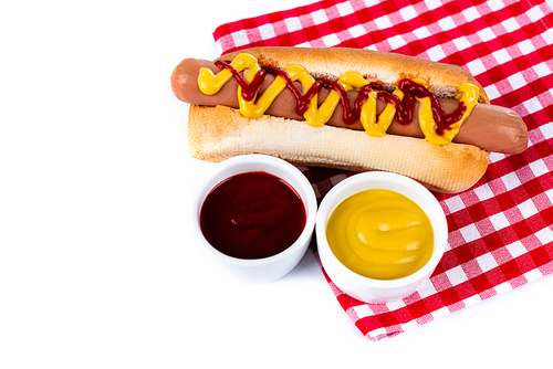 bowls with mustard and ketchup near tasty hot dog on plaid table napkin isolated on white