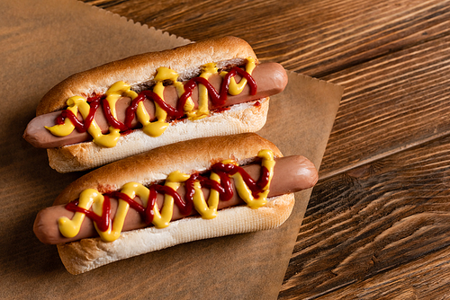 top view of delicious hot dogs and craft parchment on wooden surface