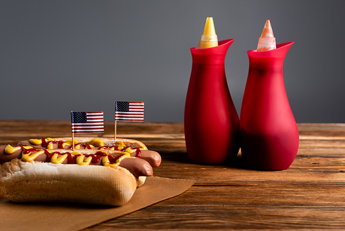 souse bottles near hot dogs with small american flags on wooden table isolated on grey