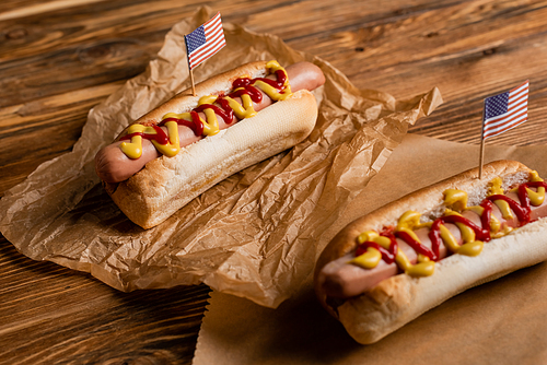 hot dogs with ketchup, mustard and small american flags on kraft paper and wooden table