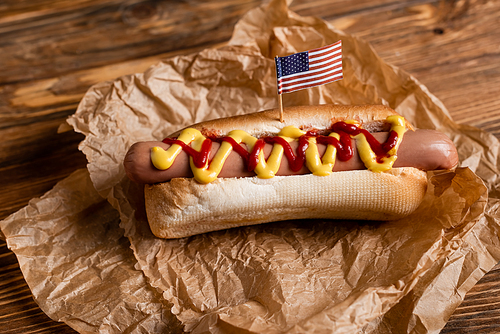 tasty hot dog with small american flag and crumpled parchment on wooden table