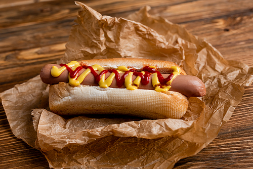 close up view of hot dog with ketchup and mustard and crumpled paper on wooden table