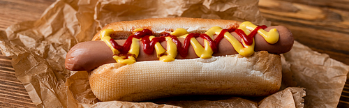 close up view of hot dog with ketchup and mustard, and crumpled kraft paper on wooden table, banner