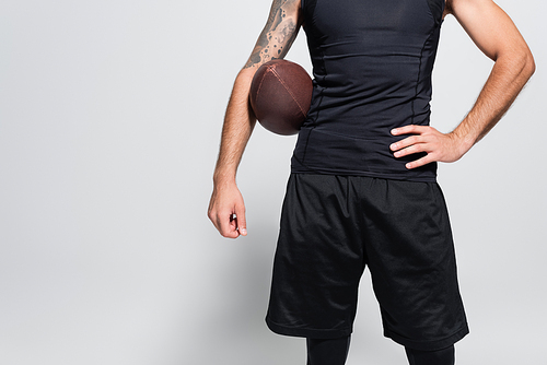 Cropped view of sportsman with rugby ball holding hand on hip on grey background
