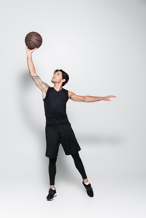 Sportsman rising basketball ball on grey background