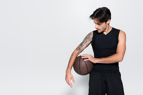 Brunette sportsman holding basketball ball on grey background