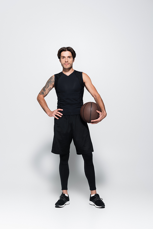 Full length of tattooed player with basketball ball  on grey background