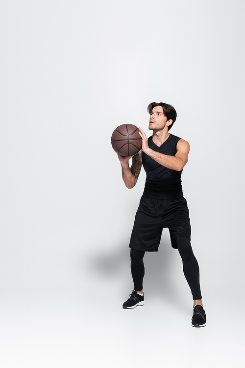 Sportsman in black sportswear playing basketball on grey background