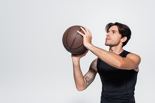 Sportsman holding basketball ball while looking away isolated on grey