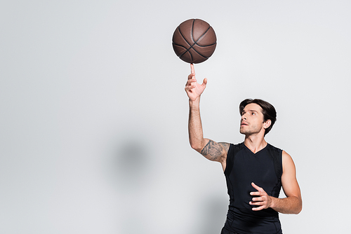 Tattooed sportsman holding basketball ball on finger on grey background