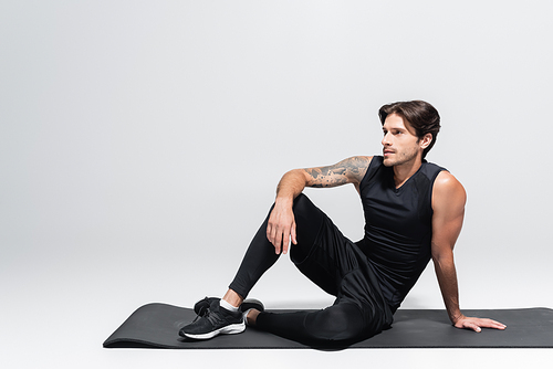 Sportsman sitting on black fitness mat on grey background