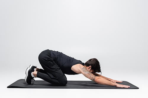 Brunette sportsman stretching on fitness mat on grey background
