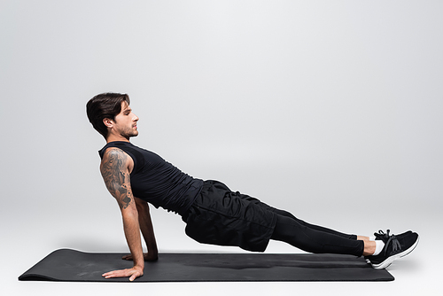 Side view of man doing plank on fitness mat on grey background