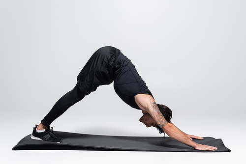 Side view of sportsman bending while stretching on fitness mat on grey background