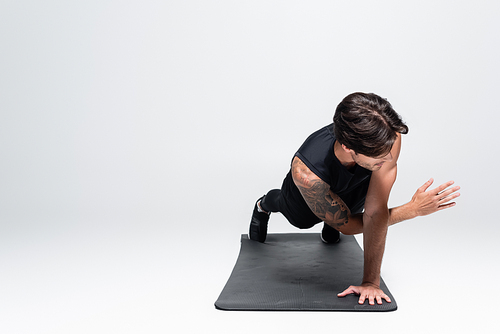 Athletic sportsman in black sportswear doing plank on fitness mat on grey background