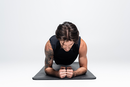 Sportsman in sleeveless shirt doing plank on fitness mat on grey background