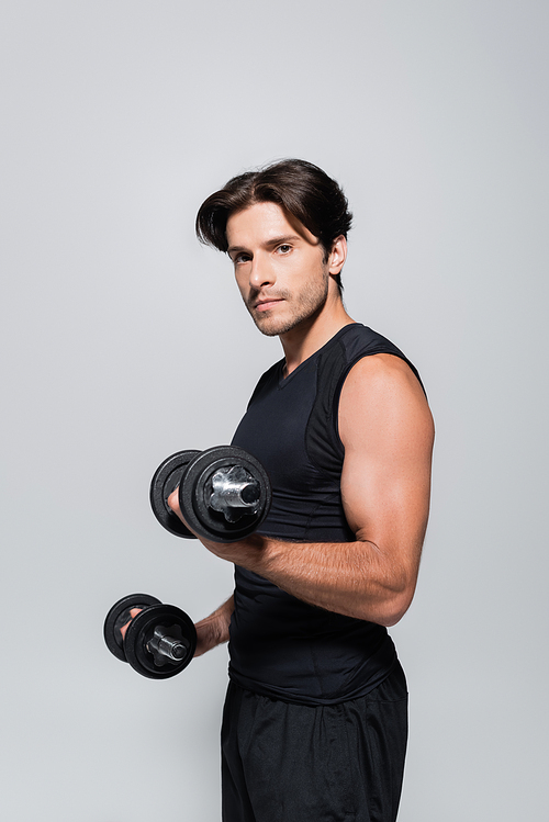 Athletic man in sportswear holding dumbbells and  isolated on grey
