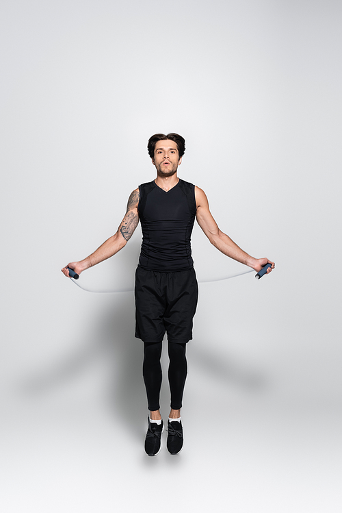 Tattooed sportsman training with jump rope on grey background