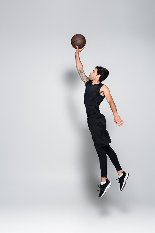 Side view of player with basketball ball jumping on grey background