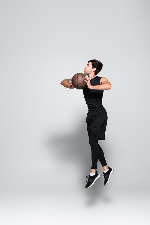 Side view of basketball player with ball jumping on grey background
