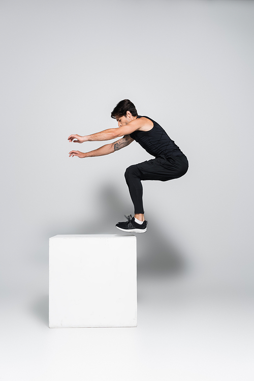 Sportsman jumping on white cube on grey background