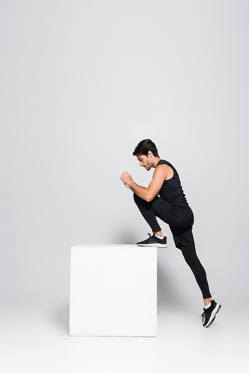 Side view of sportsman training with cube on grey background