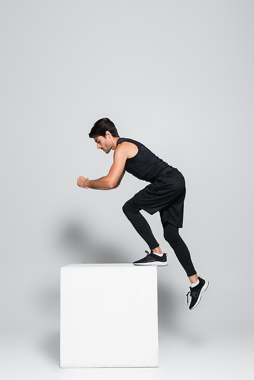 Side view of sportsman in black sportswear working out with cube on grey background