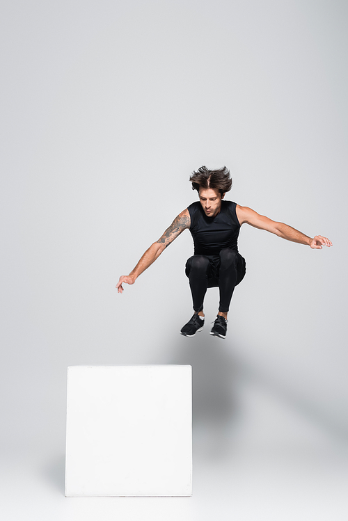 Sportsman jumping near cube on grey background