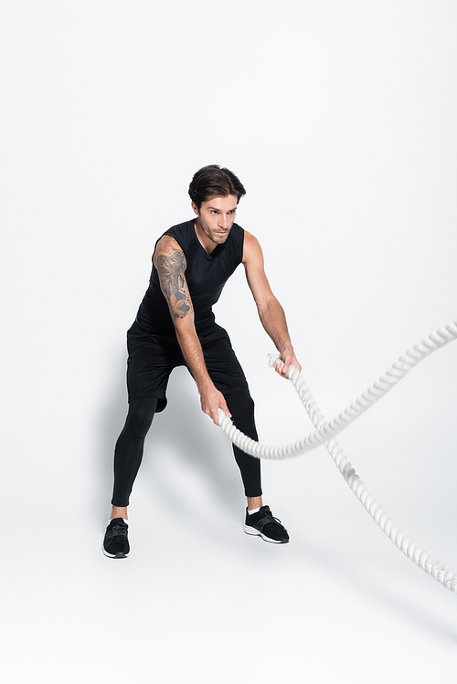 Sportsman working out with battle ropes on grey background