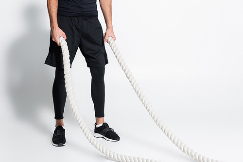 Cropped view of sportsman holding battle ropes on grey background
