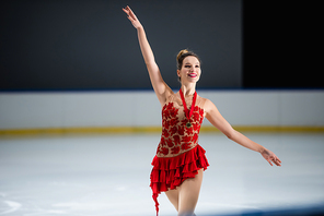 positive figure skater in red dress and golden medal gesturing on ice arena