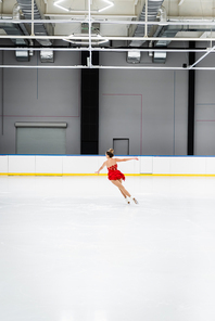 full length of young woman in dress figure skating in frozen ice arena