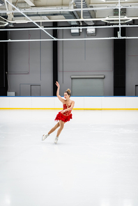 full length of young woman figure skating and gesturing in professional ice arena