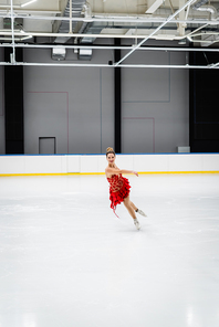 full length of joyful young woman figure skating in professional ice arena