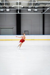 full length of woman in red dress figure skating in professional ice arena