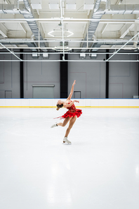full length of young woman bending while figure skating in professional ice arena