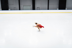 full length of woman in dress performing sit spin in professional ice arena