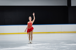 full length of happy woman with medal waving hand in professional ice arena