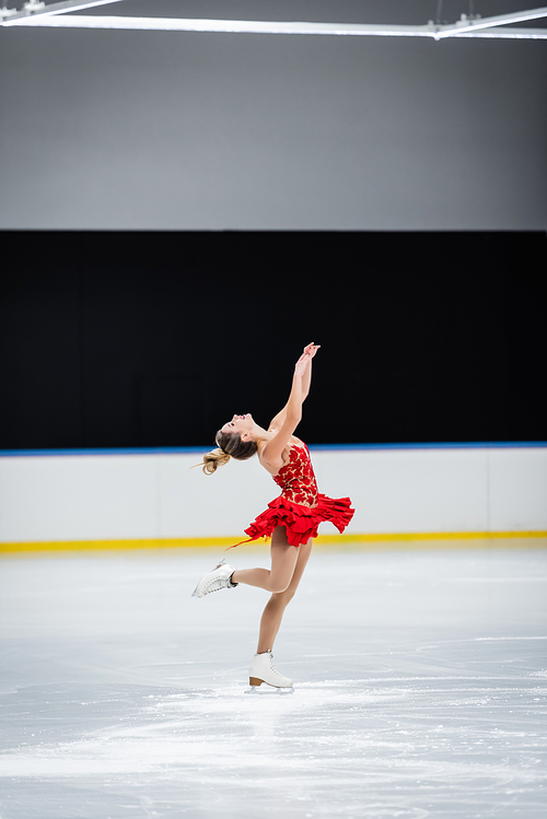 full length of happy figure skater with raised hands doing layback in professional ice arena