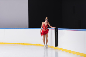 full length of worried figure skater in red dress on ice rink