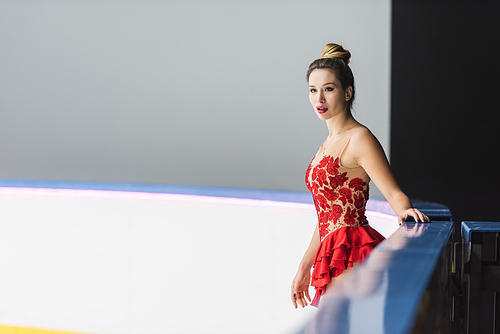 young figure skater in red dress standing on ice rink