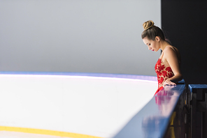 side view of young figure skater in red dress standing on ice rink